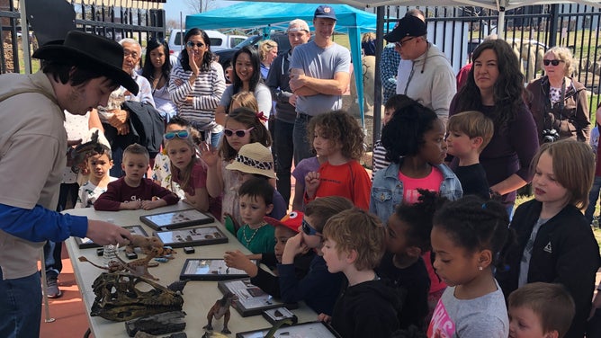 Children and adults gather around a table to learn from a park employee.