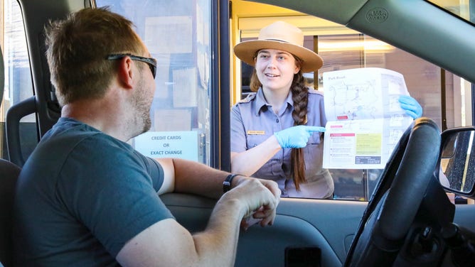 A NPS ranger points to map for a visitor sitting in his vehicle at a entrance station to Yellowstone National Park. The park is using a license plate system to keep traffic in check as the park reopens. (Image: NPS Yellowstone National Park)