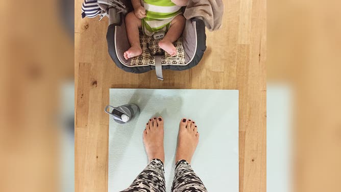 Downward point of view of woman's bare feet and baby bare feet in a Postnatal Yoga class in San Diego, California.