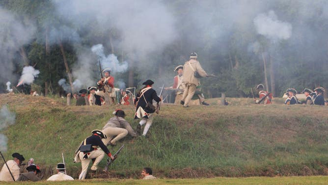 Soldier scramble up a hill while re-enacting a Revolutionary War battle.