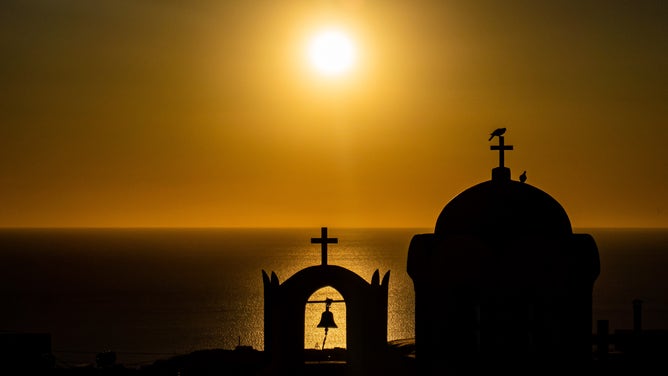 The sun rises over a church in Greece.