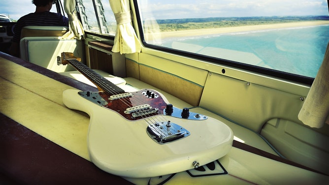 An electric guitar sits in a car, with a beach in the background.
