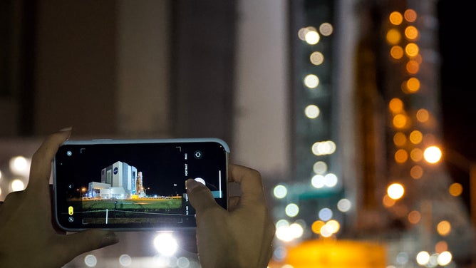 A person takes a photo of NASA's Space Launch System rocket and Orion spacecraft making the journey to Kennedy Space Center launchpad 39B on Aug. 16, 2022.