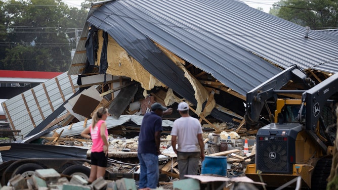 People watch cleanup efforts after buildings were destroyed by flooding on August 23, 2021 in Waverly, TN