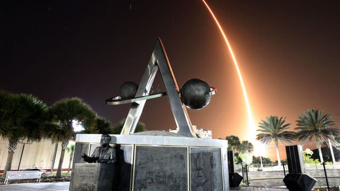 A time exposure shows the arc of the SpaceX Falcon 9 rocket as it streaks toward space after lifting off from the Kennedy Space Center, as viewed from Space View Park in Titusville, Florida on April 27, 2022. In the foreground is a monument to the Apollo space program, with a bust of former President John F. Kennedy, the sixth manned lunar mission, Apollo 16, concluded on this day exactly 50 years ago