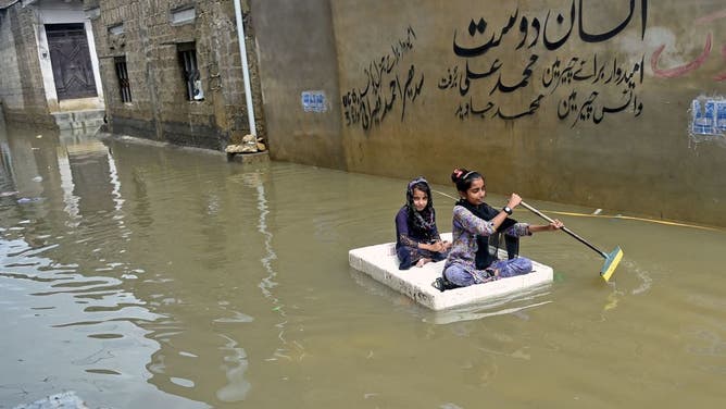 Girls use a temporary raft across a flooded street in a residential area after heavy monsoon rains in Karachi on July 26, 2022.