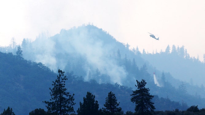A silhouette of a firefighting helicopter, as it drops water on the McKinney fire on Tuesday, Aug. 2, 2022.