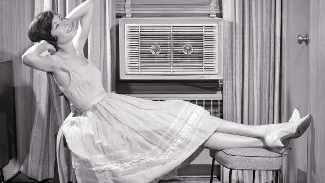 A mid-century woman relaxing in front of an air conditioning unit.