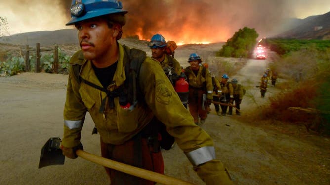 Hand crews hike out of a burning canyon as the Fairview fire approaches homes near the corner of Citrus View Drive and Fairview Avenue near Hemet on Wednesday night Sept. 7, 2022