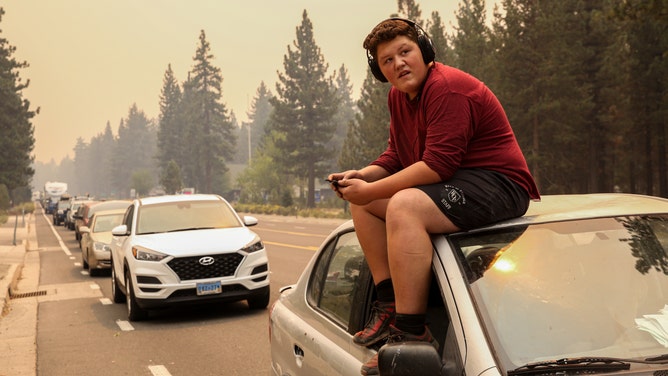 Victor Salas Jr.,15, sits on top of his car as he waits in evacuation traffic on Highway 50 out of South Lake Tahoe, Calif. on Monday, Aug. 30, 2021.