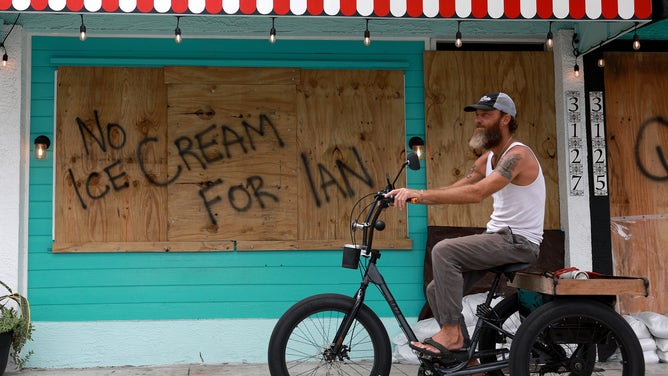 A bicyclist rides past a sign reading, 'No Ice Cream for Ian,' painted on a building that is boarded up for the possible arrival of Hurricane Ian on September 27, 2022 in St Petersburg, Florida. Ian is expected in the Tampa Bay area Wednesday night into early Thursday morning.