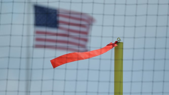 A ribbon on top of a field goal post blows in the wind, as an American flag flies in the background.