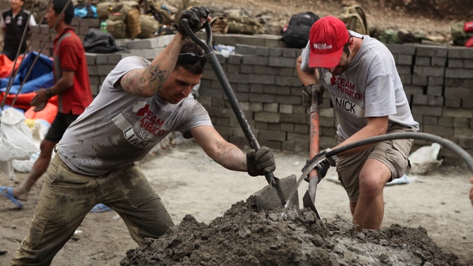 Two men with Team Rubicon mix concrete during rebuilding efforts in Nepal.