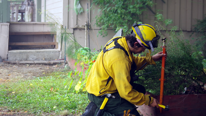 A firefighter is seen installing a sprinkler near a home in Oregon as flames from the Rum Creek Fire inch closer to residential areas.