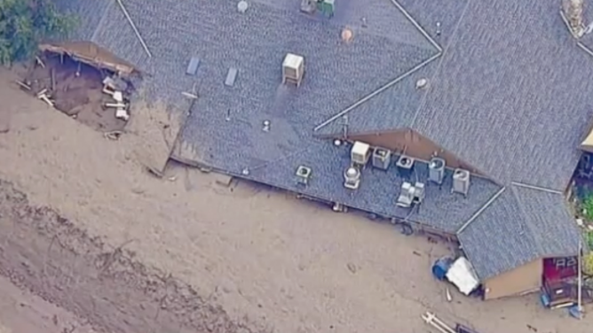 An aerial shot of a muddy debris flow reaching the rooftop of the Oak Glen Steakhouse and Saloon.