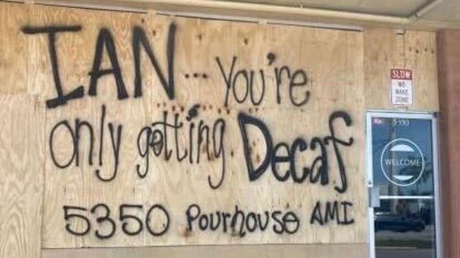 The words "IAN...You're only getting Decaf" are spray painted onto the boarded up windows of a restaurant in Manatee County, Florida.
