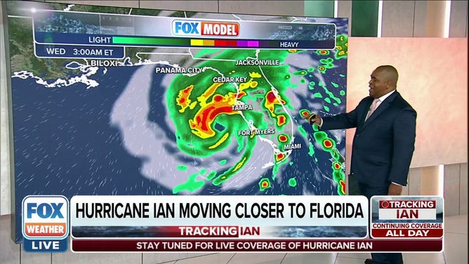 Man stands next to monitor showing Hurricane Ian nearing Florida