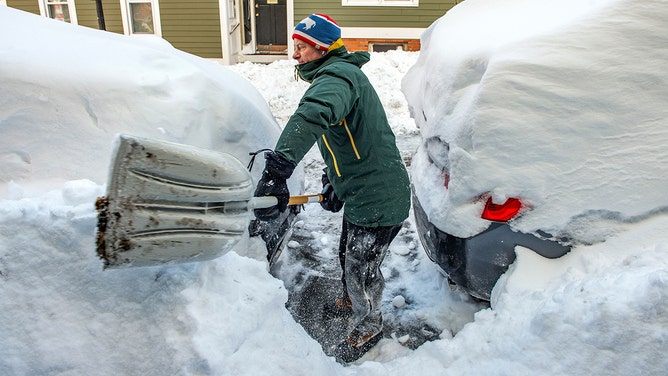 FILE - A resident shovels snow around vehicles in Boston, Massachusetts, on January 30, 2022.