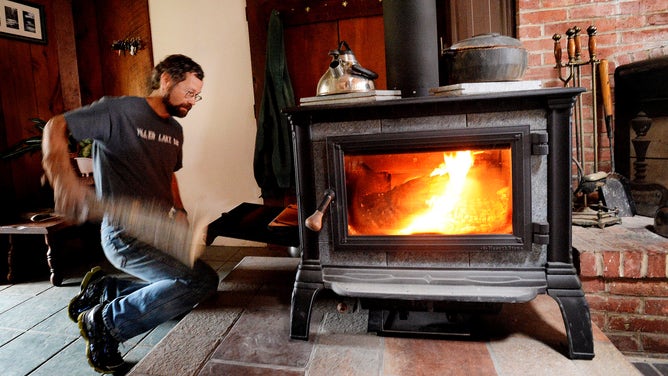 A man feeds his wood stove. 