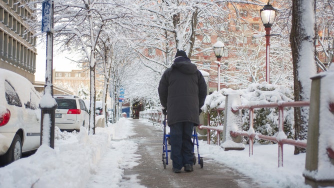 An older man walks along a snowy sidewalk.