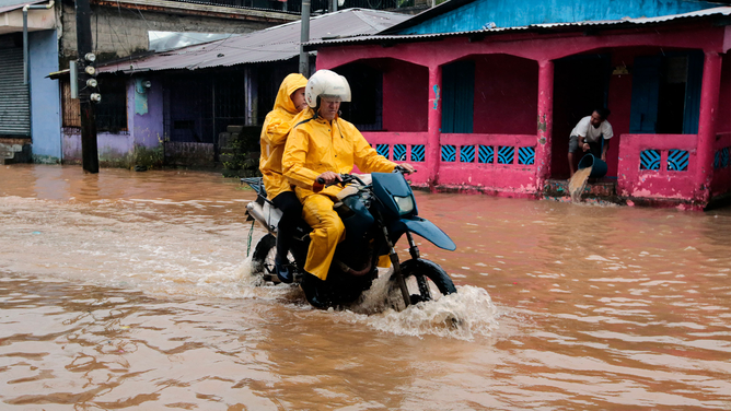 Residents ride on motorbike in a flooded street following the passage of Hurricane Julia in the town of Bluefields, on the Caribbean coast of Nicaragua on October 9, 2022. - Hurricane Julia raked across Nicaragua Sunday, lashing the country with winds and heavy rain and bringing potentially life-threatening flash flooding and mudslides to much of Central America.