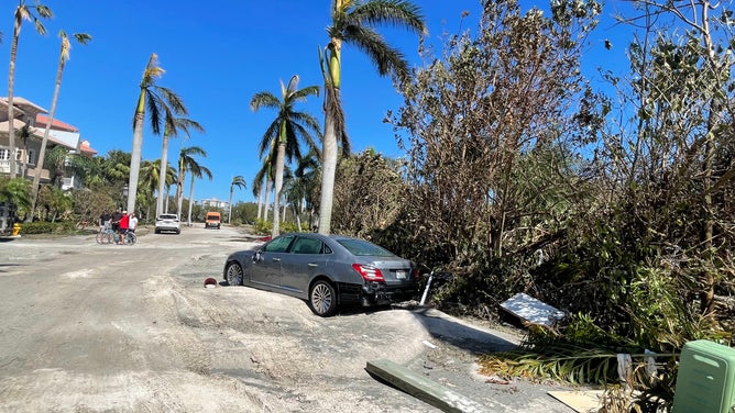 The storm surge left behind tattered trees and piles of sand on the road, and floated cars into the mangroves.