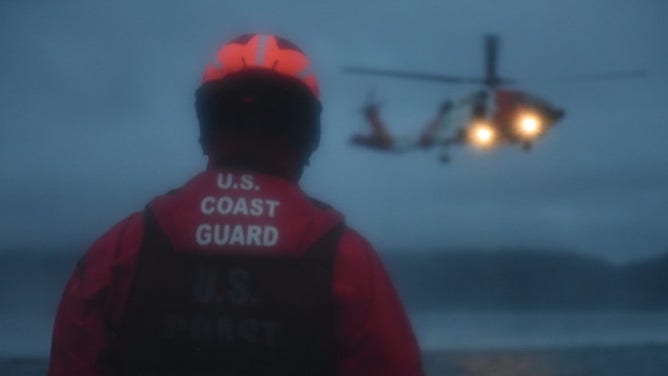 A Coast Guard machinery technician watches a Coast Guard Air Station Sitka MH-60 Jayhawk helicopter.