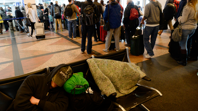 FILE - DENVER, CO - March 24: A man tries to sleep as hundreds of airline passengers line up at the United Airlines ticket counters at Denver International Airport March 24, 2016. Thousands of passengers that were stranded at the airport due to Wednesday's blizzard are finally being able to take off after a complete shutdown of the airport.
