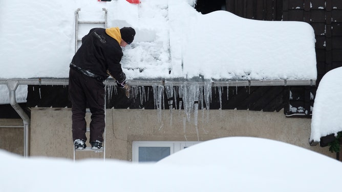 A man removes icicles from the gutter of a house.