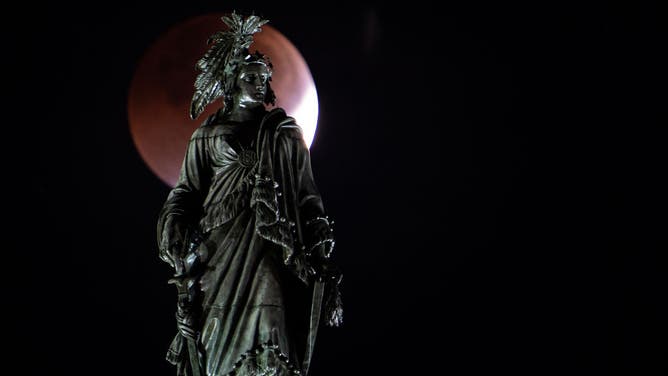 The Election Day blood moon lunar eclipse is seen behind the Statue of Freedom atop the U.S. Capitol dome on Tuesday morning, November, 8, 2022.