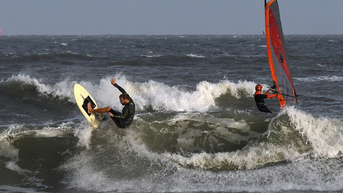 A surfer and a windsurfer enjoy the rough waves at Cocoa Beach, Florida, as Tropical Storm Nicole approaches the east coast of Florida.