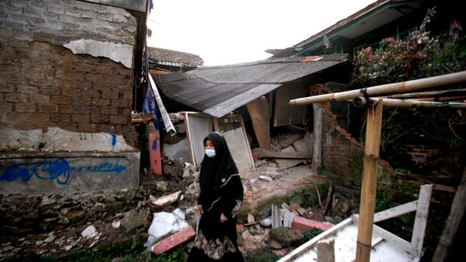 A woman walks past a damaged house following an earthquake in Cianjur on November 21, 2022. - At least 56 people were killed in an earthquake that rattled Indonesia's main island of Java on November 21, 2022, the governor of the worst-hit province said.