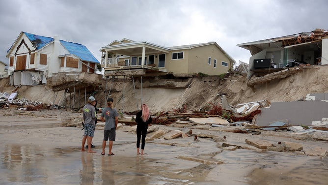 People look on at homes that are partially toppled onto the beach after Hurricane Nicole came ashore on November 10, 2022 in Daytona Beach, Florida.