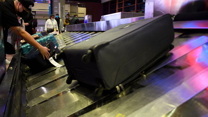 FILE - Airline passengers wearing face masks wait to collect bags from a baggage carousel at the Harry Reid International Airport (LAS) on January 2, 2022 in Las Vegas.