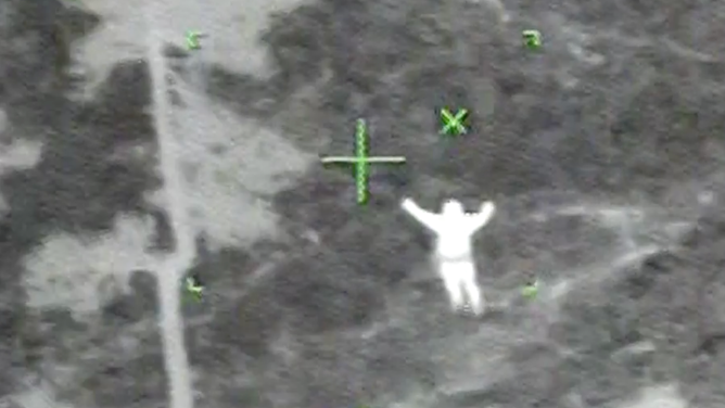 Irving Langmaid stands with his arms raised to catch the attention of the U.S. Coast Guard helicopter crew.