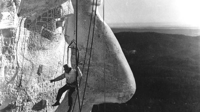 The face of Abraham Lincoln under construction on Mount Rushmore in 1936 with Gutzon Borglum monitoring the work.