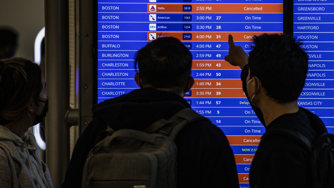 FILE - Travelers look at flight timetables displayed on a departure board at Ronald Reagan National Airport (DCA) in Arlington, Virginia, U.S., on Sunday, Jan. 16, 2022.