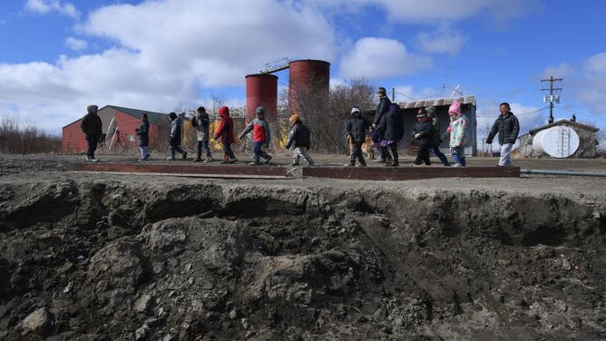 Schoolchildren walk beside severe erosion of the permafrost tundra next to their school at the climate change affected Yupik Eskimo village of Napakiak on the Yukon Delta in Alaska on April 18, 2019.