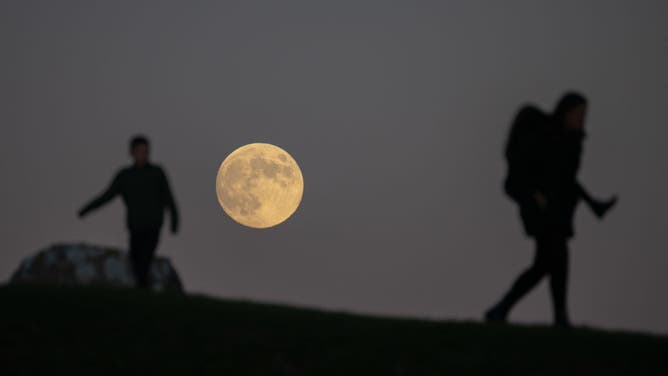 Children play to the backdrop of the full moon, known as the Cold Moon as it rises, on December 07, 2022 in Portland, England