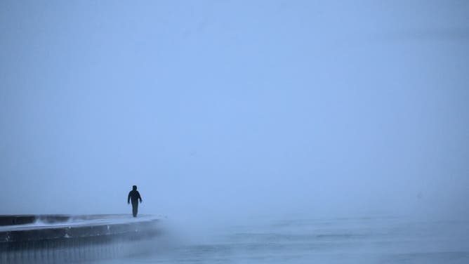 A man walks along Lake Michigan at sunrise as temperatures hover about -8 degrees on December 22, 2022 in Chicago, Illinois. Sub-zero temperatures are expected to grip the city for the next couple of days with wind chill temperature dipping as low as -40 degrees. (Photo by Scott Olson/Getty Images)