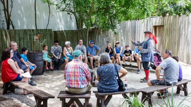 A guide in period clothing talking to families at the Colonial Quarter living history museum.