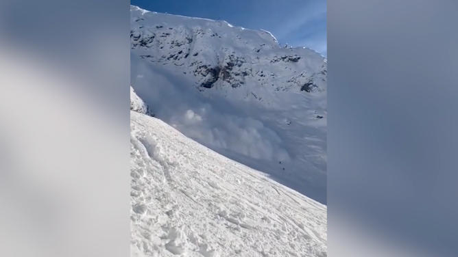 The avalanche swallows up the skiers, who appear as tiny black figures on the white snow.