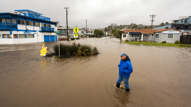 A pedestiran wades through a flooded neighborhood in Aptos, California, US, on Saturday, Jan. 14, 2023. Storm-weary California is bracing for new round of drenching rains, heavy snowfall and dangerous winds as the death toll from a series of atmospheric rivers reached 19 people.
