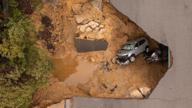 In an aerial view, a car and a pickup truck are seen inside a sinkhole as another storm created by a series of atmospheric rivers inundates California on January 10, 2023 in Los Angeles, California. Two vehicles containing four people fell into the sinkhole which had opened up under the road they were driving on during heavy rainfall in the the suburban Los Angeles neighborhood of Chatsworth.