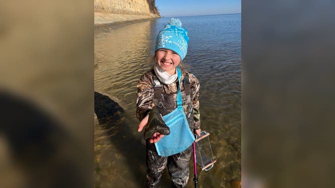 Molly Sampson holding the Megalodon tooth by a Calvert County beach on the Chesapeake Bay.