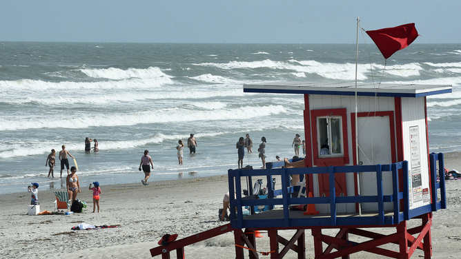 FILE - A high hazard red flag is flown at a lifeguard tower as beach-goers enjoy the rough surf generated by the Tropical Storm Humberto as it moves north off the coast of Florida.