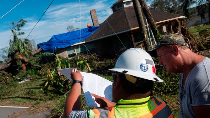 An electric company employee along with a local resident surveys the damage done to the power lines next to a large tree that fell on a house following the passage of hurricane Laura in Lake Charles in Louisiana on August 27, 2020.