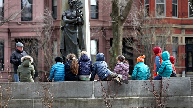 Winter coats were needed instead of short sleeves for these local school students seated by a sculpture on the Commonwealth Mall in Boston during an exceptionally cold spring day on March 28, 2022.