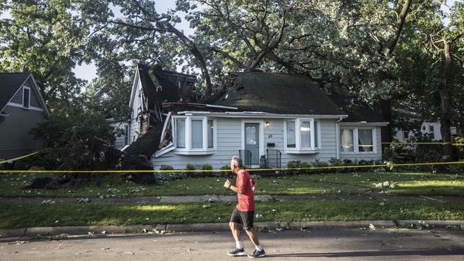 A person jogs past a large tree that fell on the roof of a home in the Chicago area on June 14, 2022.