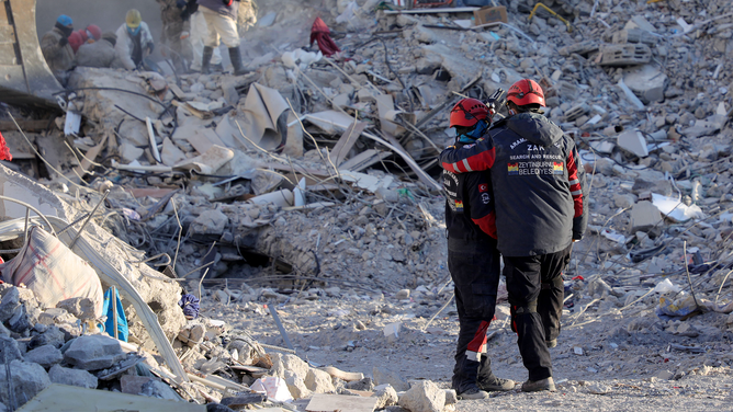 Members of the Zeytinburnu Municipality Search and Rescue Team (ZAK) confort themselves by the rubble of collapsed buildings in Nurdagi, near Gaziantep, on February 13, 2023, as rescue teams began to wind down the search for survivors, a week after an earthquake devastated parts of Turkey and Syria leaving more than 35,000 dead and millions in dire need of aid.